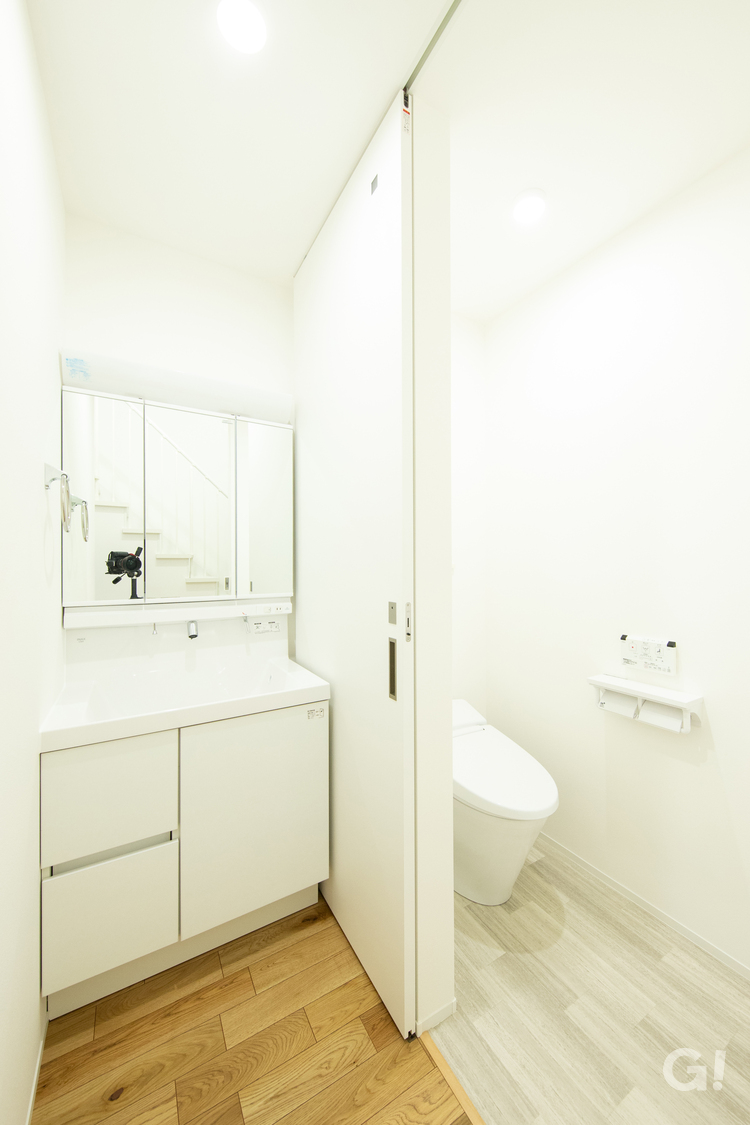 『白で明るく清潔感漂う空間！引き戸で仕切られたトイレへも続くシンプルな洗面室』の写真