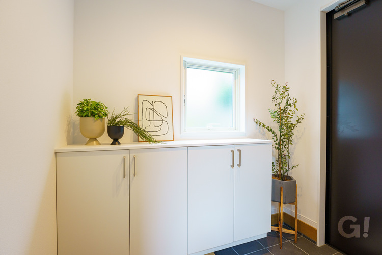 『白で統一され清潔感あふれる空間◎グリーンが美しく映えるシンプルモダンな玄関』の写真