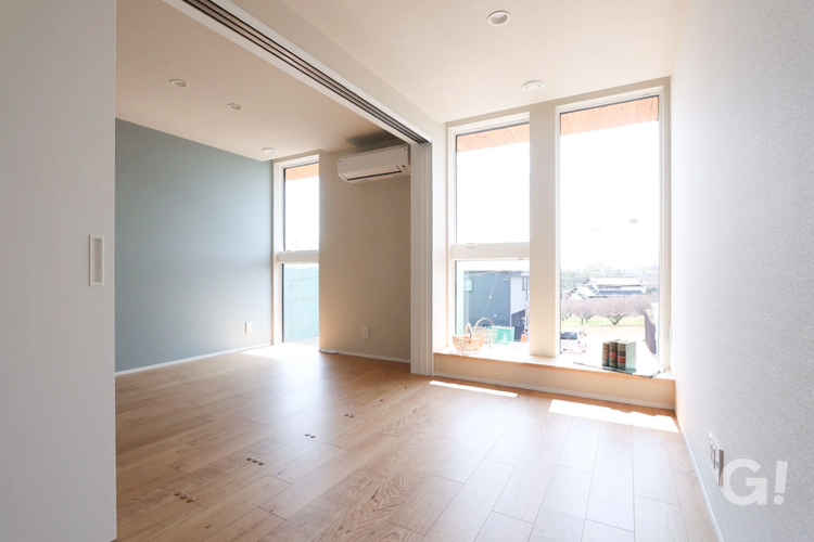 千葉県市川市の注文住宅にある、開放的で明るい2階フリースペース。ブルーグレーのアクセントウォールとナチュラルな木目調フローリングが特徴的。大きな窓からは外の景色を借景として楽しめ、窓辺にはカウンターが設けられている。読書やリモートワーク、趣味の部屋として多