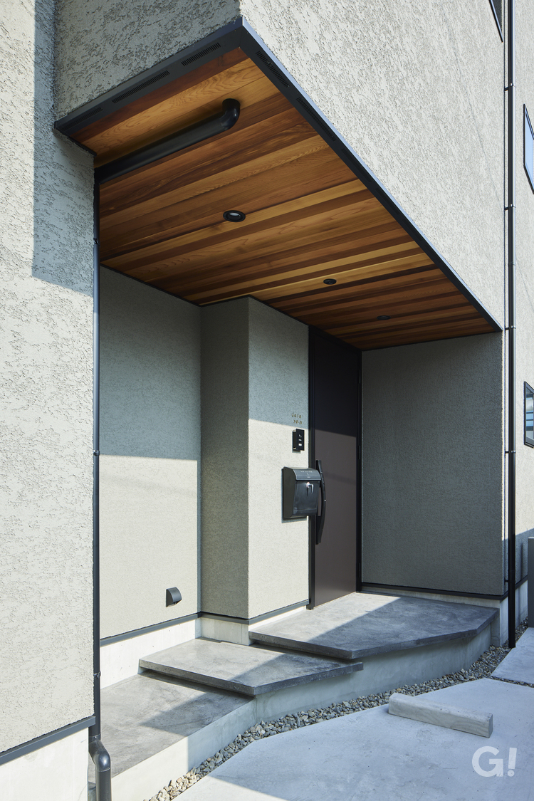 『グレーの塗り壁×美しい木目が映えるモダンなデザイナーズ住宅の玄関ポーチ』の写真