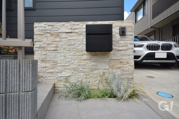 凹凸感のあるベージュ系の石壁が美しいナチュラルな家の玄関アプローチ