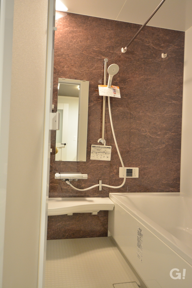 『大理石風のブラウンの壁が高級感漂い美しいナチュラルな家の浴室』の写真