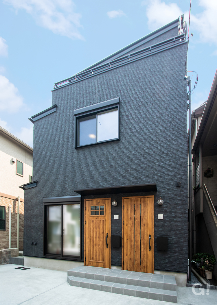 マットな黒いサイディングの外壁に、木目のドアがアクセントとして映えるシンプルで洗練された外観