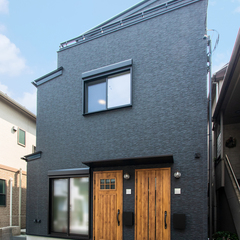 マットな黒いサイディングの外壁に、木目のドアがアクセントとして映えるシンプルで洗練された外観