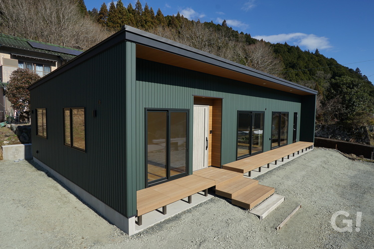 外壁のダークグリーンのガルバリウムと木目が調和したシンプルモダンな平屋。 木目調の軒天が優しい表情を添え、ウッドデッキと一体化した玄関ポーチが内と外をつなぎます。